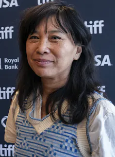 A woman in a vest smiles against a navy background.
