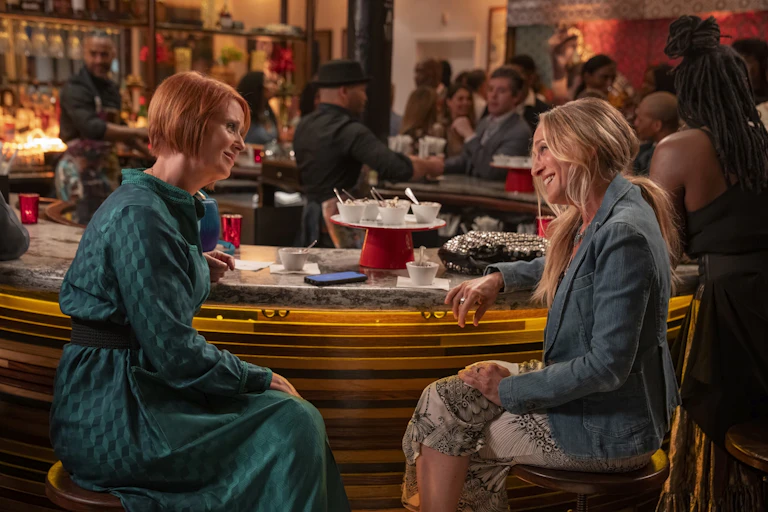 Screenshot from a television show of two white woman having a conversation at a table in a restaurant