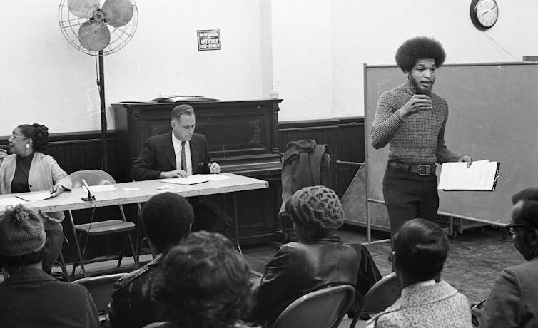 Young man with afro speaks to local residents.