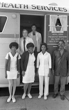 Six people pose next to a mobile facility.