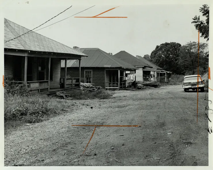 Black and white photo of old, one-story homes along a dirt road.