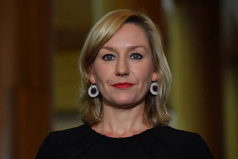 Stern faced blonde woman wearing large earrings and a black top.
