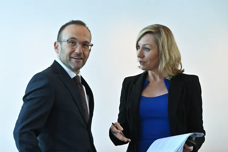 Man wearing a suit and glasses listens to a woman in a blue top and dark jacket