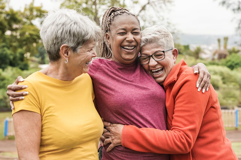 Three women in colourful tops laugh and hug
