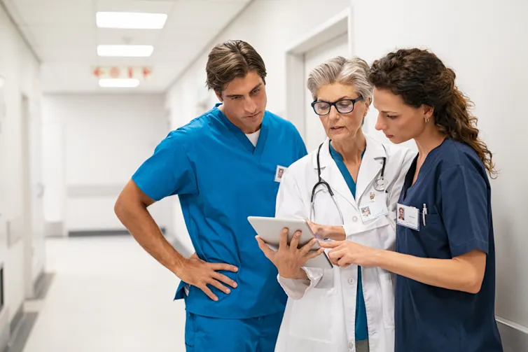 Three health workers consult electronic tablet in hospital corridor