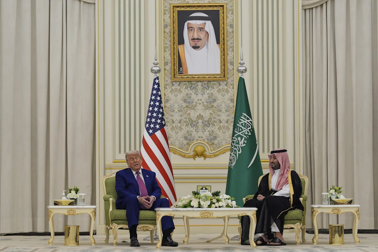 Two men speak in an opulent cream room.