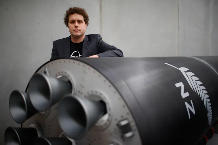 Peter Beck standing behind a large rocket painted in black with a fern.