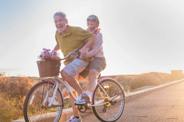 An older, laughing couple ride on a bike together in sunshine