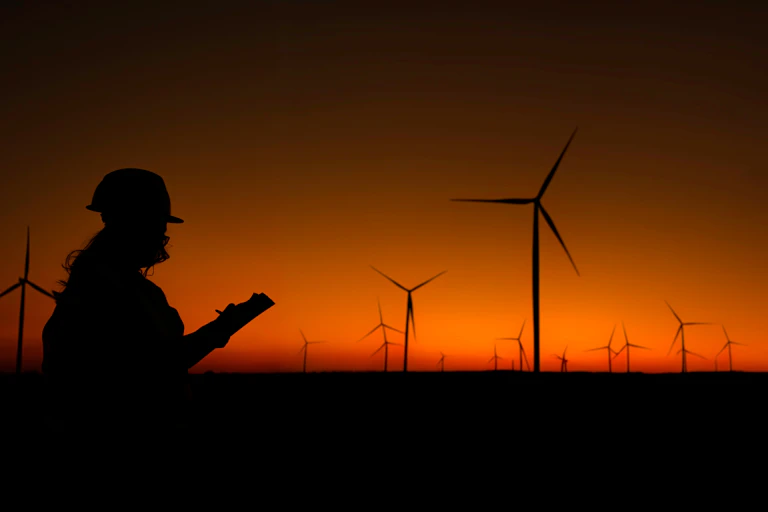 A silhouette of an engineer surveying a wind farm at dusk.
