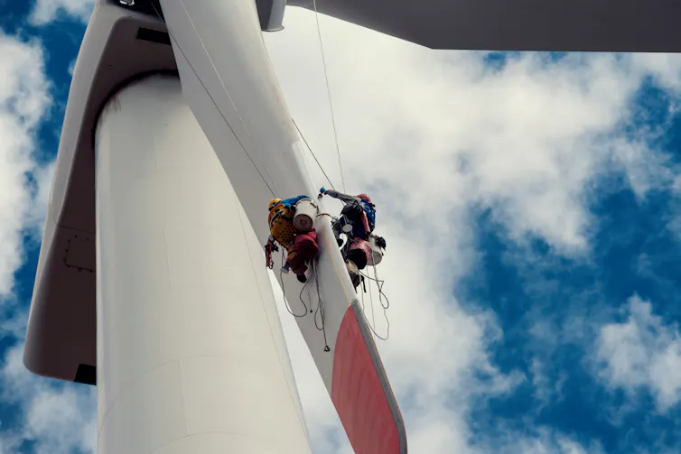 Workers abseiling down a wind turbine blade.