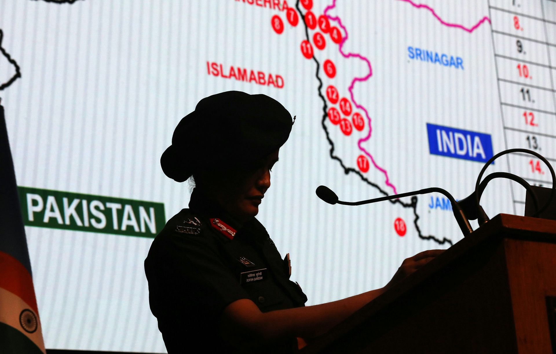 Woman in military uniform stands in between lectern and map of India-Pakistan border.