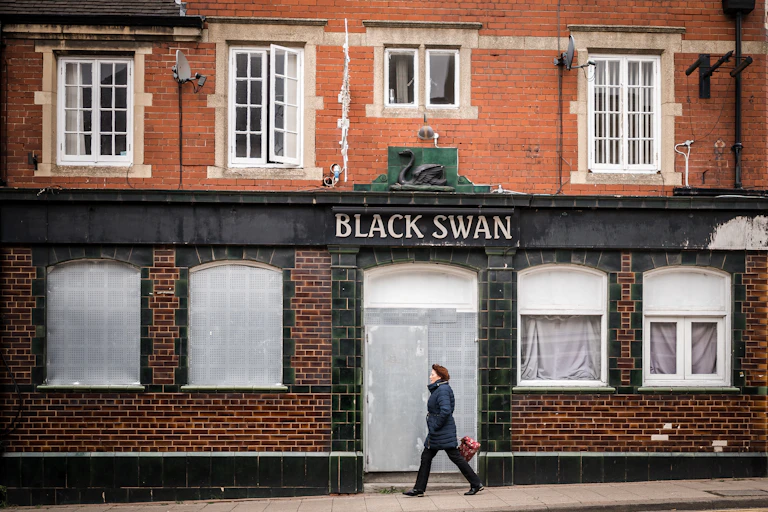 A woman walks past a boarded up pub called the Black Swan