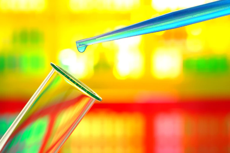 Laboratory pipette with drop of blue liquid over glass test tube