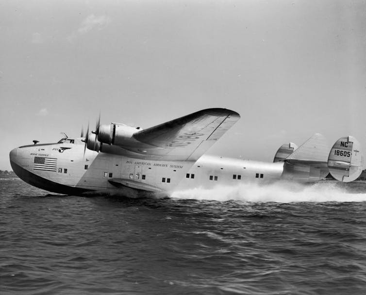 Black-and-white photo of a sea plane landing on water.