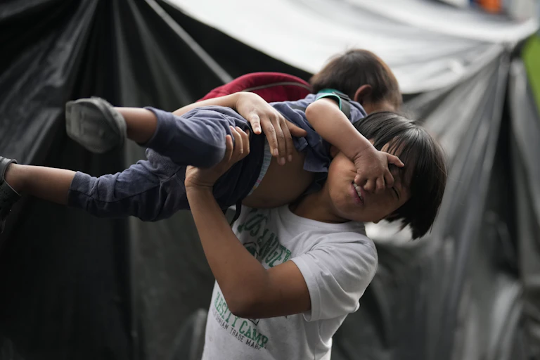 A child picks up a toddler over his head.