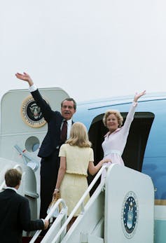 Man in suit and a woman wave right before they board a plane.