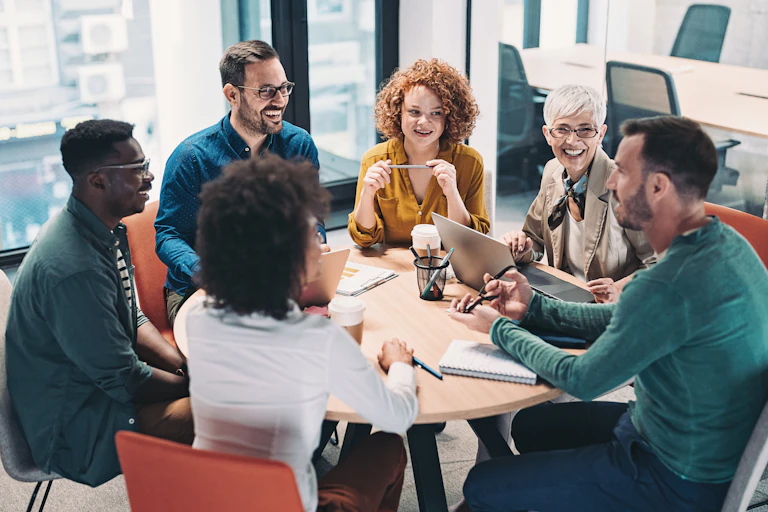 Half a dozen businesspeople speak around a round table.