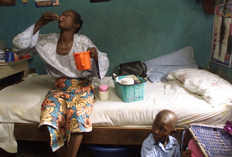 Mother sitting on bed taking medications with young son sitting near her