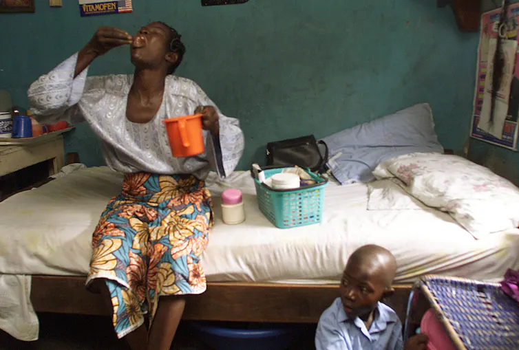 Mother sitting on bed taking medications with young son sitting near her