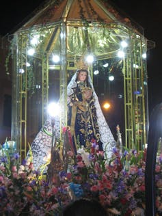 An image of the Virgin Mary, surrounded by flowers placed at her feet, and lights glowing around her.