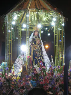 An image of the Virgin Mary, surrounded by flowers placed at her feet, and lights glowing around her.