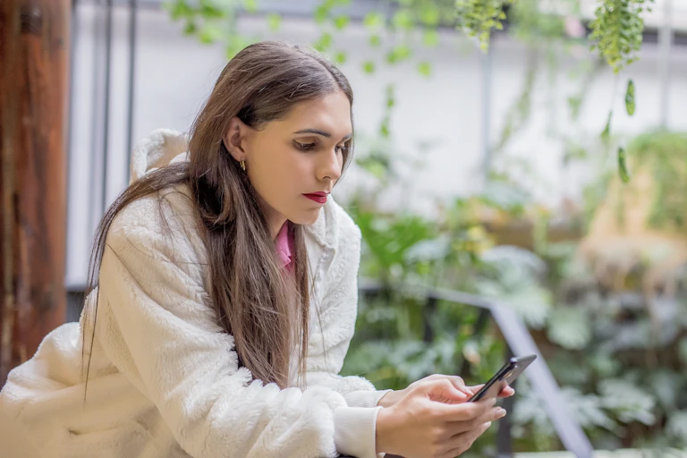 A young trans woman in her garden looks at her phone