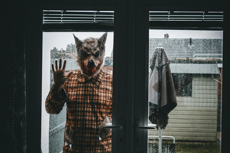 A man in a wolf mask outside, pressing up against glass door to the inside