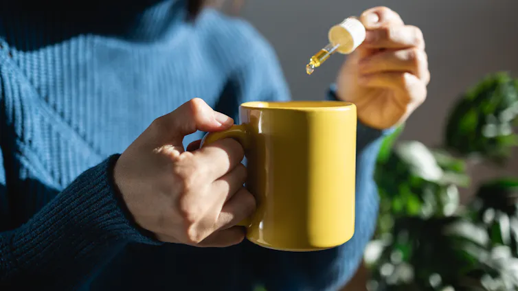 Woman's hands drop CBD oil into a yellow mug.