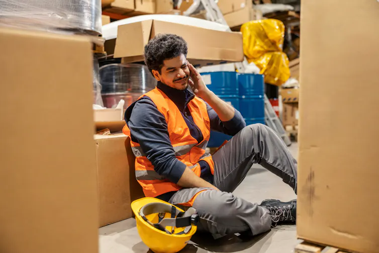 Construction worker sits among boxes in warehouse.