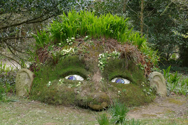 a giant head with grass hair rising out the ground