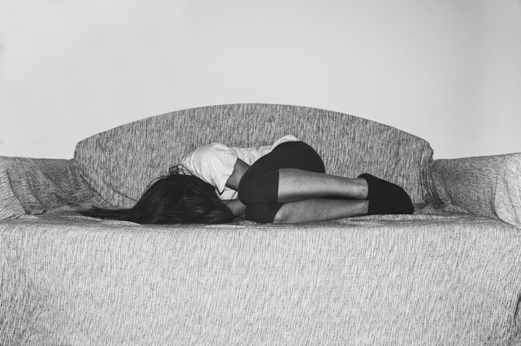 A woman curls up in pain on a couch.