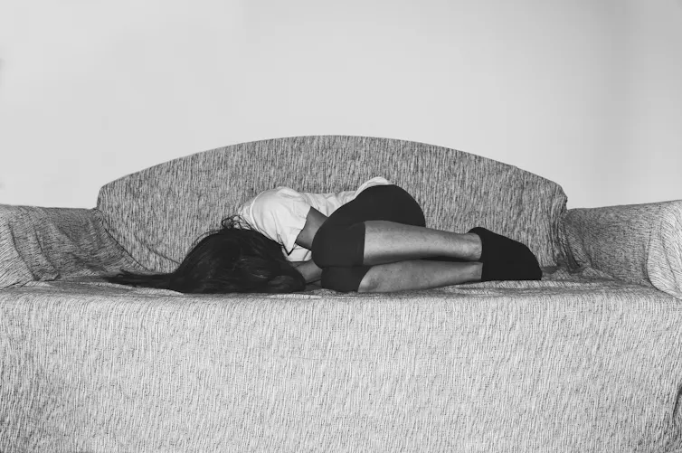 A woman curls up in pain on a couch.
