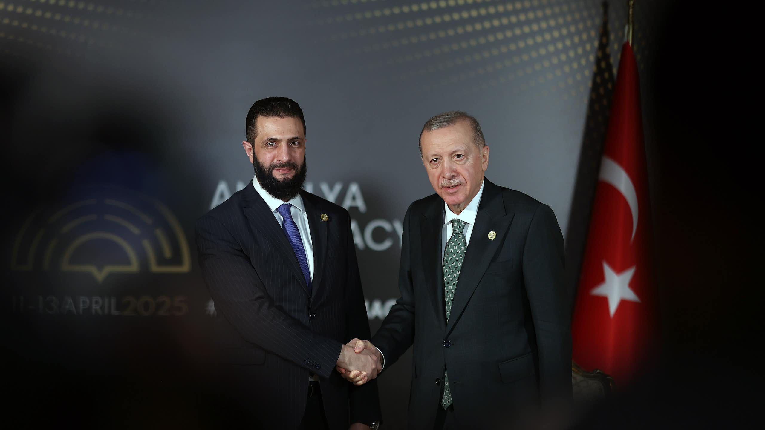 Two men in suits shake hands for a photo.