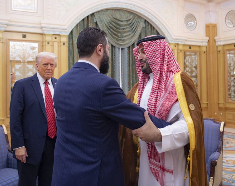 Three men greet in a room.