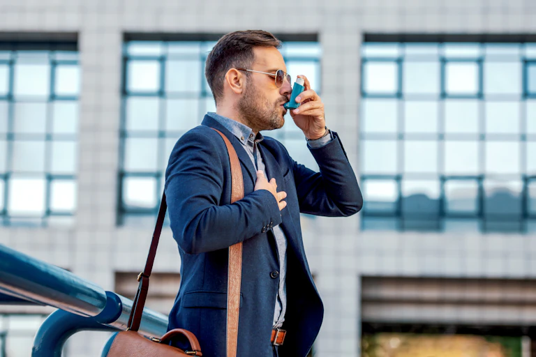 A man wearing sunglasses and a suit in the city uses an asthma inhaler.
