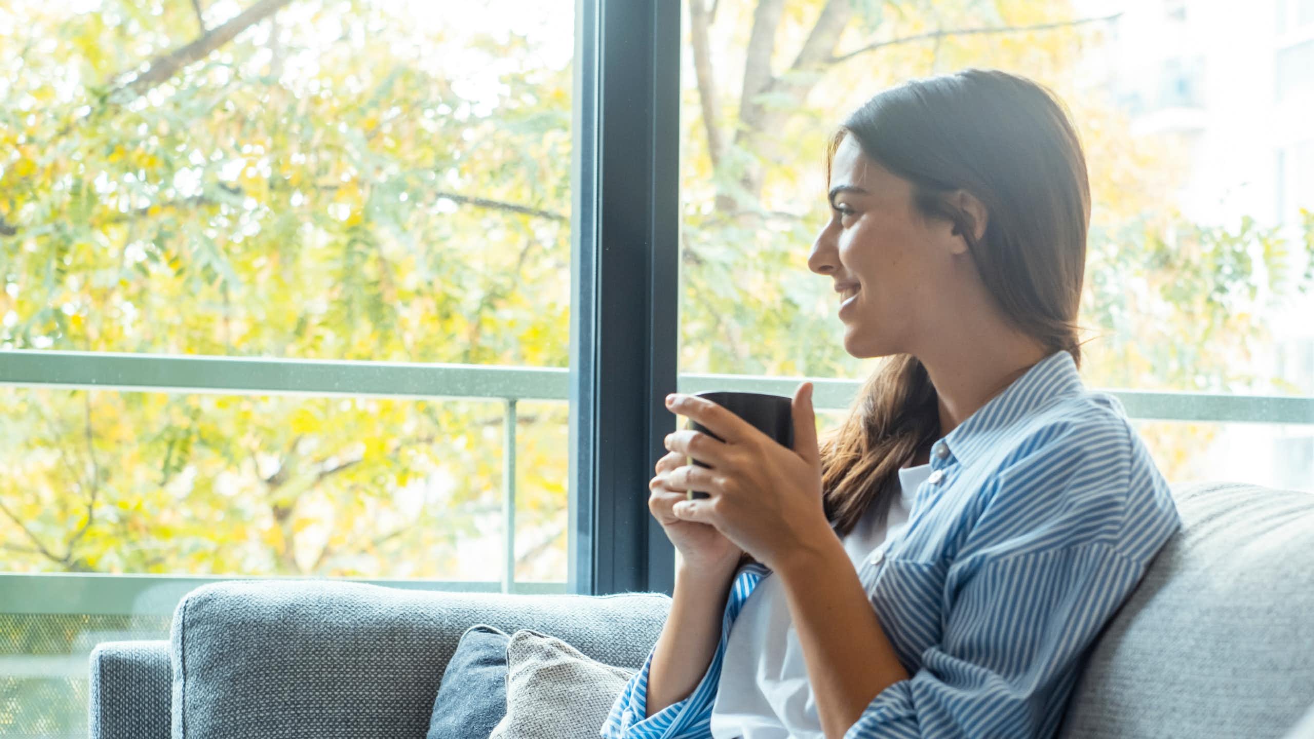 Une jeune femme assise sur un canapé en train de boire une tasse de café.