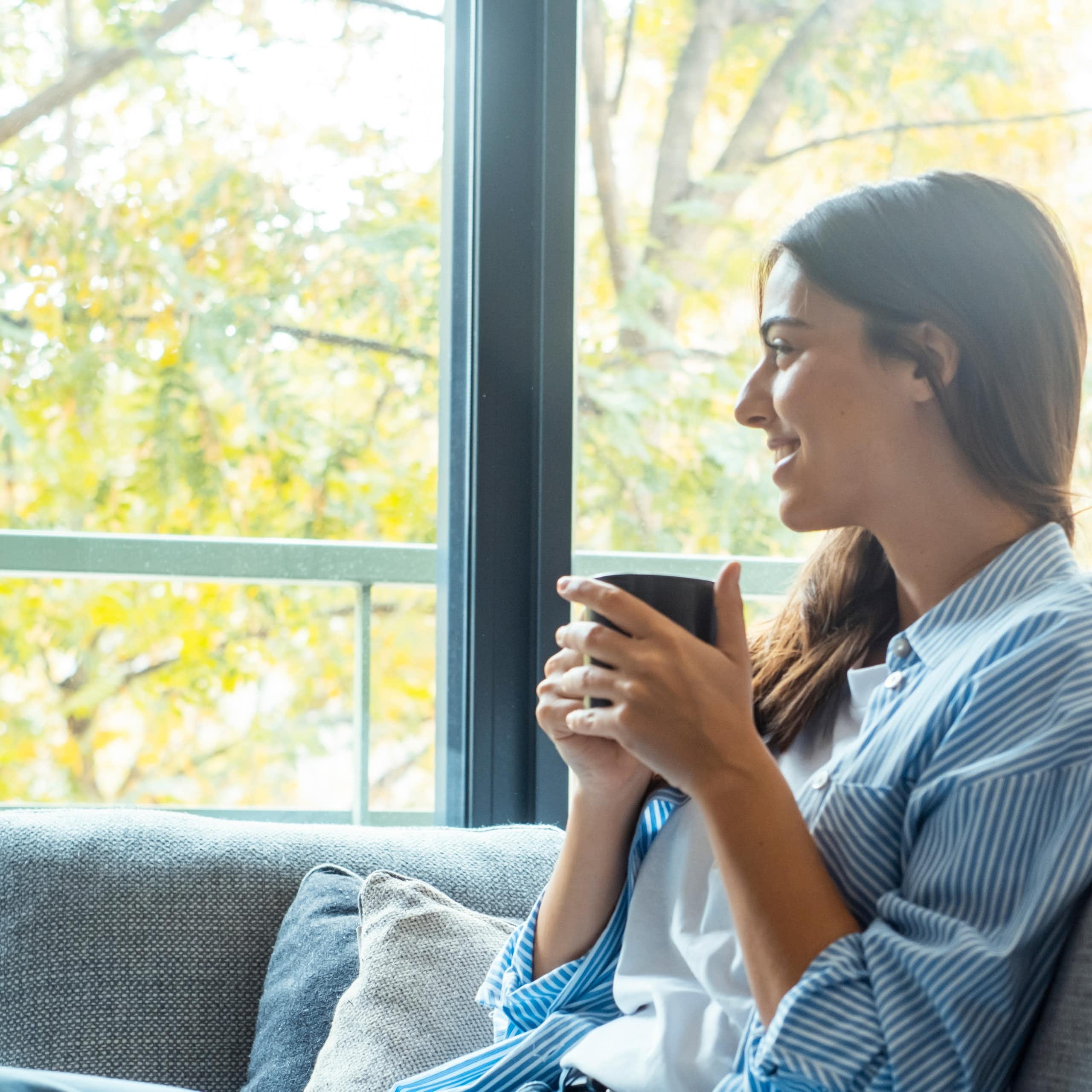 Une jeune femme assise sur un canapé en train de boire une tasse de café.