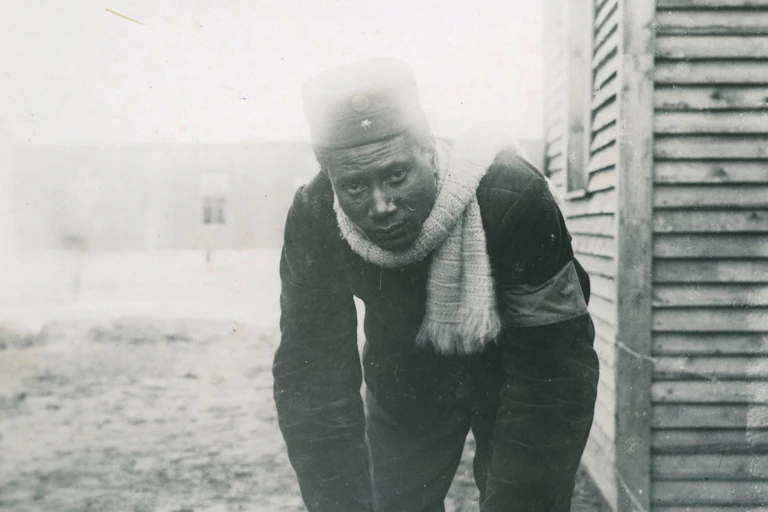 An old black and white photograph of an African man looking grimly at camera, dressed in warm clothes.