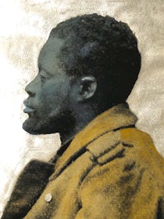 A colourised portrait in profile of an unsmiling African man with a beard in a thick brown coat.