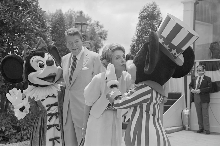 An older couple being embraced by Mickey and Minnie Mouse.
