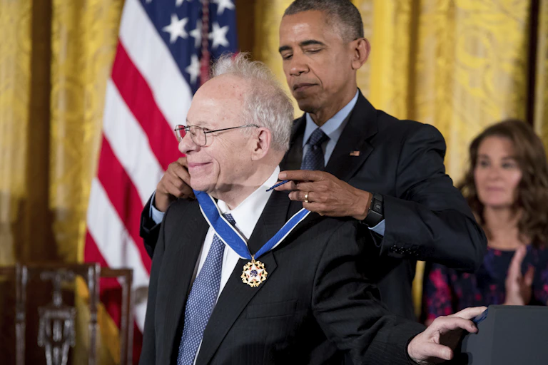 a tall middle-aged man places a medal around the neck of a shorter older man