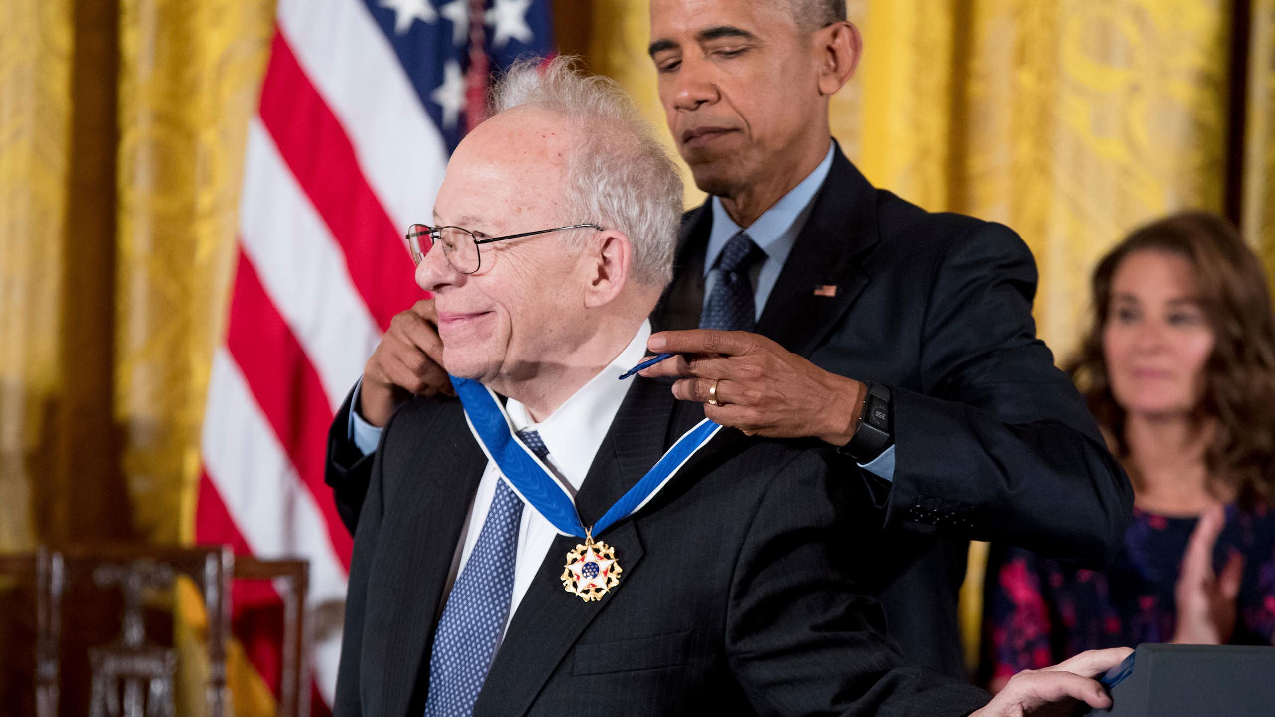 a tall middle-aged man places a medal around the neck of a shorter older man