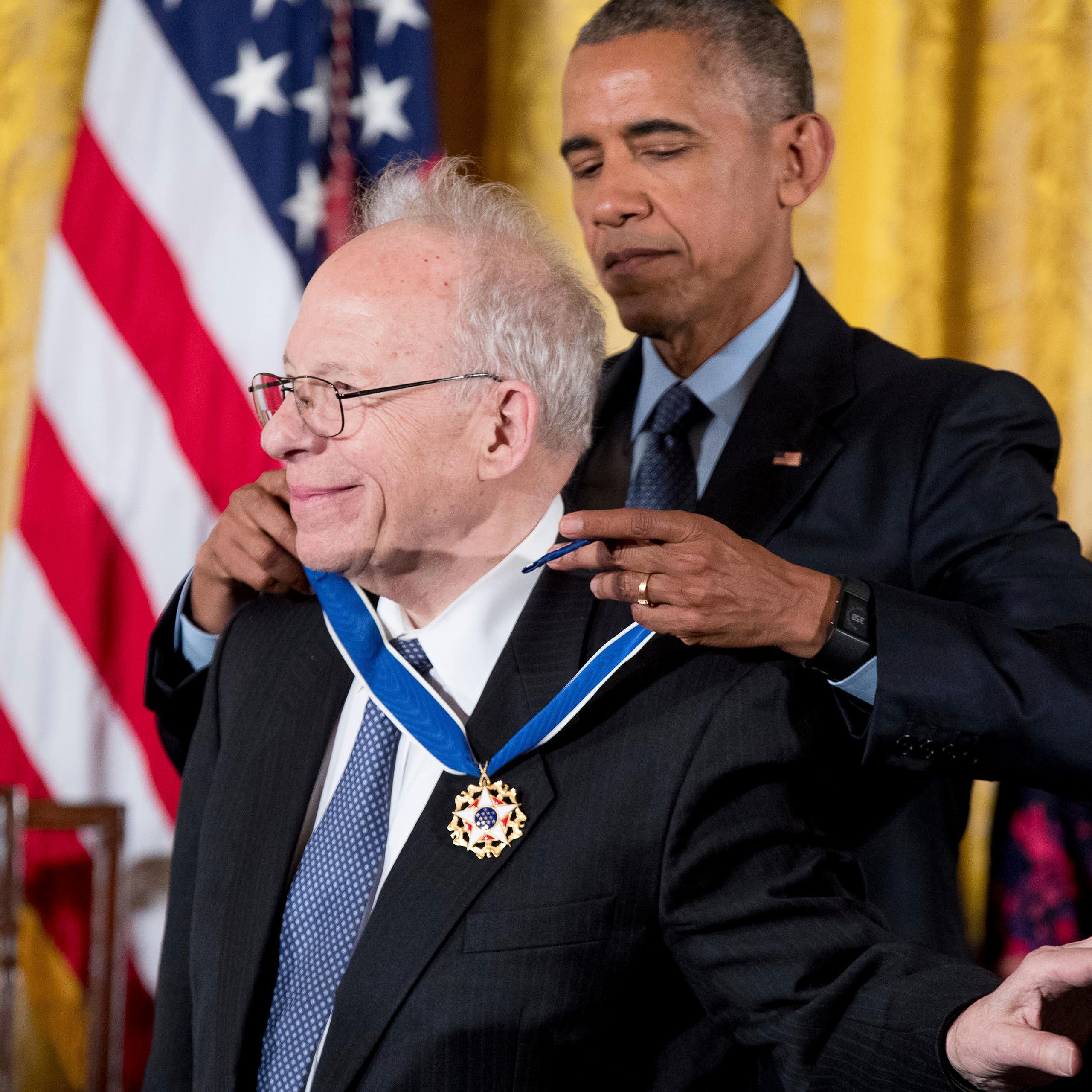 a tall middle-aged man places a medal around the neck of a shorter older man