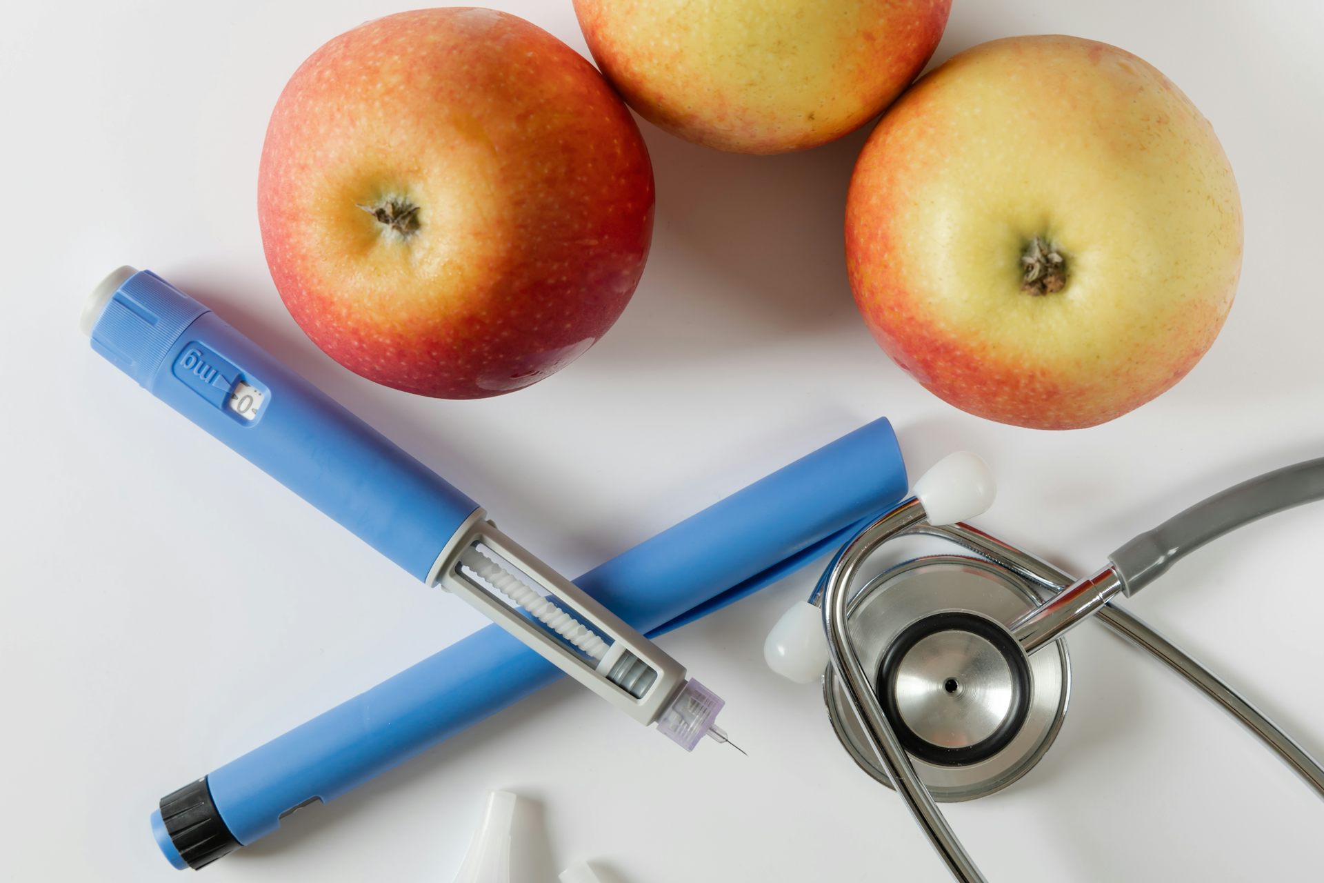 Photo d'archive montrant deux stylos injecteurs de semaglutide bleus, un stéthoscope et trois pommes.