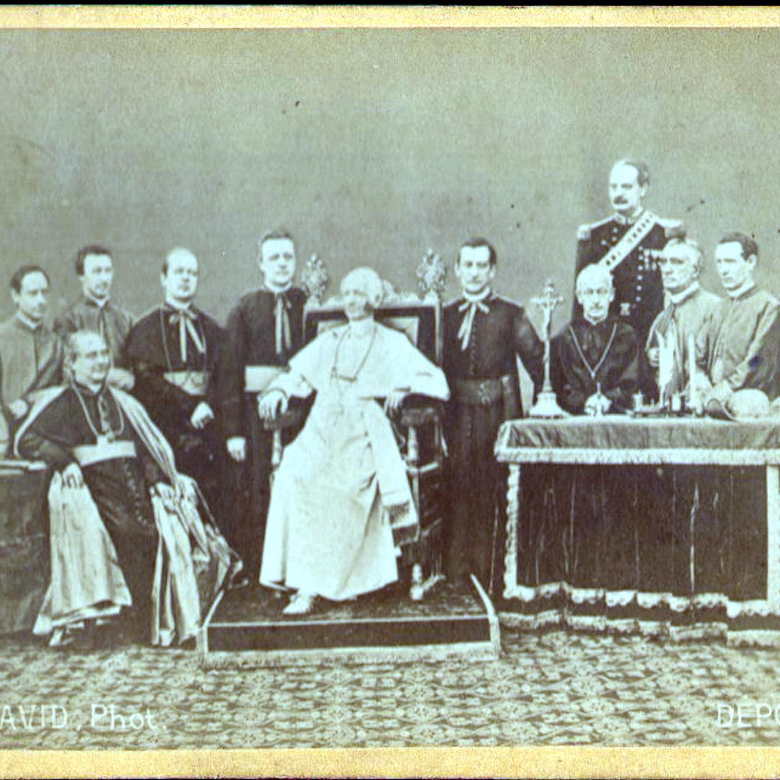 A faded, black and white photograph of a handful of men formally posed around a man dressed in white who sits on a throne.