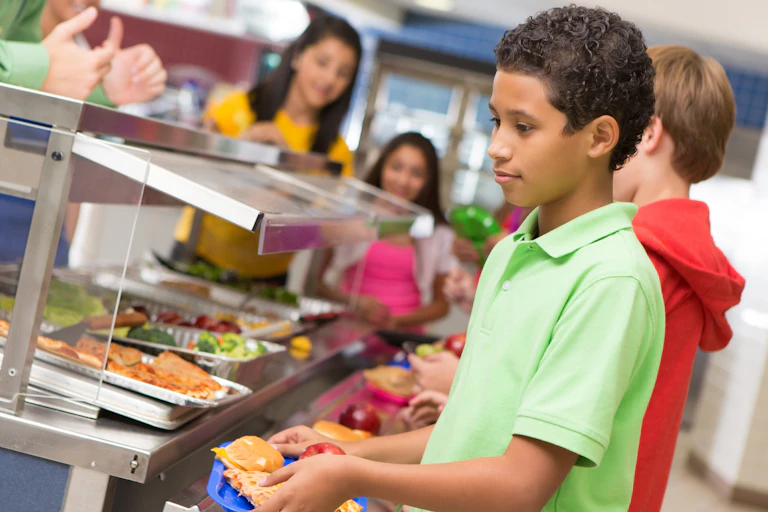A middle school boy stands in line at his school cafeteria.