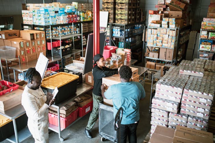 Inside a food bank filled with canned goods and packages, a group of volunteers process donations.