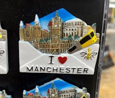 A fridge magnet featuring an image of the city emerging from an envelope that reads I heart Manchester, and has a bee on it