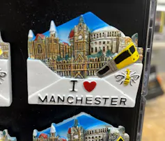 A fridge magnet featuring an image of the city emerging from an envelope that reads I heart Manchester, and has a bee on it