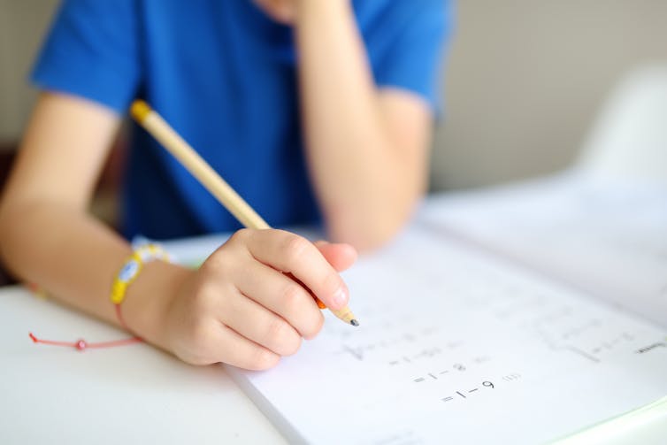 Young boy writes on a maths workbook.